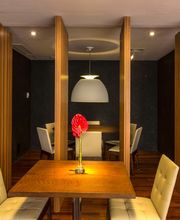 Sala de jantar moderna com madeira, cadeiras brancas e luminária central acima da mesa.