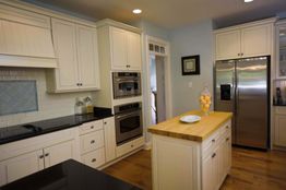 Modern kitchen with white cabinets, wood island, stainless steel appliances, and recessed lighting.