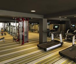 Gimnasio moderno con cintas de correr, pesas y equipos diversos en una sala amplia y bien iluminada.