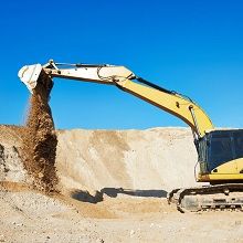 Excavator moving dirt in a sunny construction site against a clear blue sky.