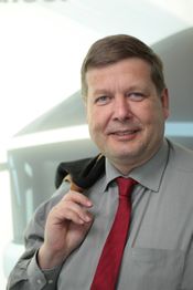 Ein Mann im Hemd und roter Krawatte trägt ein Jackett über der Schulter und lächelt.