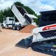 Dump truck unloading sand next to a Bobcat on a construction site.