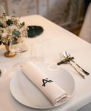 Mesa elegante con plato, servilleta, cubiertos y copa de vino; centro de mesa con flores.