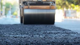 Close-up of a steamroller paving a road with fresh asphalt under bright daylight.