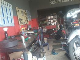 Oficina mecânica com ferramentas, moto em manutenção e prateleiras ao fundo.