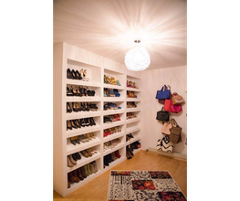 Begehbarer Kleiderschrank mit Regalen voller Schuhe und Taschen, Teppich auf dem Boden.