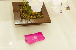 Orquídeas brancas em vaso quadrado ao lado de cartões rosa sobre a mesa.