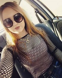 Eine Frau mit Sonnenbrille im Auto, trägt ein Netzoberteil und schaut in die Kamera.