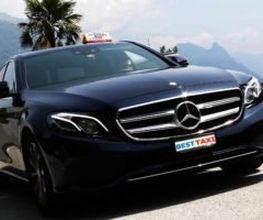 Schwarzes Mercedes-Taxi vor einer Bergkulisse mit Palmen im Hintergrund.