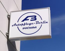 Gebäudewand mit einem Schild mit der Aufschrift: "Autopflege-Berlin PRIMM", blauer Himmel im Hintergrund.