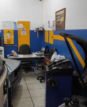 Oficina automotiva com carro, bancadas, cadeiras, e ferramentas; paredes azul e amarelo.