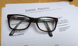 Brille auf Anwaltsdokumenten mit dem Namen "Simone Pertschi", Kontaktinformationen sichtbar.