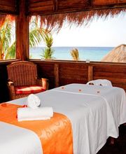 Camas de masaje con vista al mar, en cabaña de madera decorada con toallas y pétalos.