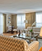 Sala de estar elegante com sofás, mesa de vidro e luminária acesa. Cortinas claras ao fundo.