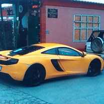 Gelber Sportwagen parkt vor einem Gebäude mit orangener Fassade und schwarzem Schild.