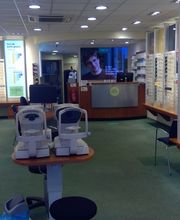 Optiekzaak met brillen op planken, oogtestapparaten en een balie aan de achterkant.