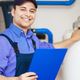 Tecnico sorridente con cappello blu tiene una cartellina vicino a un'apparecchiatura industriale.