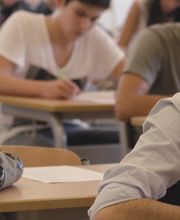 Studierende sitzen an Tischen in einem Klassenzimmer und schreiben aufmerksam während einer Prüfung.