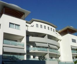 Moderne, mehrstöckige Wohnanlage mit weißen Fassaden und großen Balkonen unter blauem Himmel.
