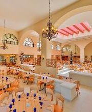 Restaurante amplio con mesas de madera, techos altos, arcos y lámparas colgantes elegantes.