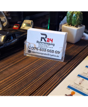 Ein Modellauto neben einer Visitenkarte auf einem Holztisch, mit einem kleinen Kaktus im Hintergrund.