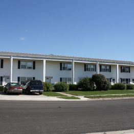 Row of white townhouses with parked cars and clear blue sky.