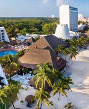 Vista aérea de un complejo hotelero junto a la playa, rodeado de palmeras y piscina.
