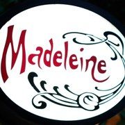 Placa oval com a palavra "Madeleine" em vermelho, decorada com arabescos pretos e azuis.