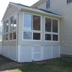 A small sunroom with large windows attached to a beige house.