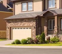 Modern stone house with a two-car garage, surrounded by green shrubs.