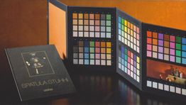 Campionario di colori con pieghevole aperto e copertina nera su fondo arancione.