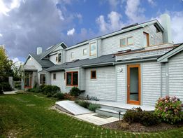 Modern house with gray siding, large windows, and a garden under a partly cloudy sky.