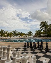 Vista de una piscina rodeada de palmeras y un tablero de ajedrez gigante al frente.