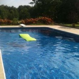 Pool with a lime green float, surrounded by greenery under a clear sky.