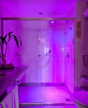 Banheiro com iluminação roxa, espelho amplo, vaso sanitário e chuveiro com box de vidro.