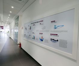 Corredor de escritório com um quadro informativo na parede, refletindo luz suave.