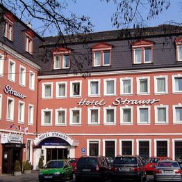 Rotes Hotelgebäude mit Schriftzug "Hotel Strauss", Autos parken davor.