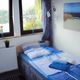 Kleines Schlafzimmer mit Bett, Fensterblick auf See, blau-weiße Bettwäsche, Pflanzen und Bild.