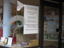 Praxisschild mit Angeboten wie Therapie, Gewichtsreduktion, Massagen in einem Fenster.