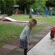 Meisje speelt minigolf op grasveld terwijl mensen op de achtergrond toekijken.