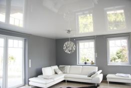 Modernes Wohnzimmer mit weißer Couch, grauen Wänden, großer Fensterfront und hängender Lampe.