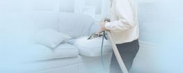 Person cleaning a sofa cushion with a vacuum cleaner in a softly lit room.