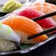 Close-up of sushi assortment with chopsticks, featuring salmon, tuna, and wasabi on a dark plate.