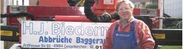 Person in Arbeitskleidung steht vor einem Fahrzeug mit Schild "H.J. Biedermann Abbrüche Baggerarbeiten".