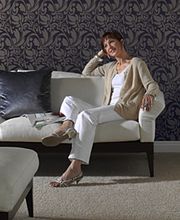 Frau sitzt im eleganten Wohnzimmer auf einem weißen Sofa, umgeben von stilvollem Dekor und Tapeten.