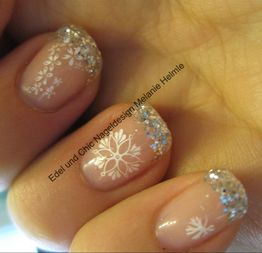 Nahaufnahme von Fingernägeln mit glitzernder French-Manicure und weißem Schneeflockendesign.
