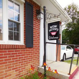 Red brick building with a sign saying "New Patients Welcome" and a small garden in front.