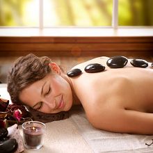 Woman enjoying a hot stone massage, relaxed, with candles nearby, in a tranquil spa setting.
