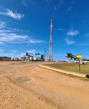 Estrada de terra direcionada a um parque industrial com céu azul e algumas nuvens ao fundo.