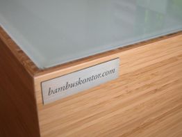 Holztisch mit Glasoberfläche und Metallschild mit der Aufschrift "bambuskontor.com".